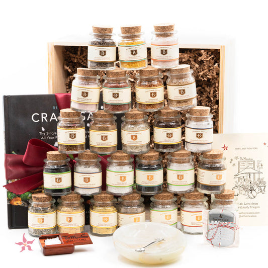 A gift set of Around the World Salt, featuring multiple small glass jars of salt, each with a different label, arranged in a wooden box. Accompanied by a pewter salt spoon, a pocket box, and other salt-related items.