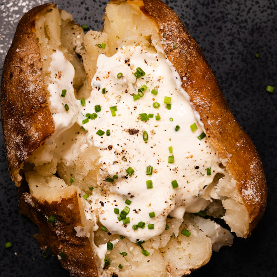Baked potato with sour cream and chives and sour cream and onion salt on a dark surface