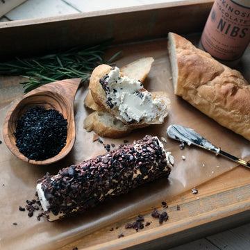 Wooden board with bread, spread, and chocolate-covered treat on a rustic surface with black diamond salt