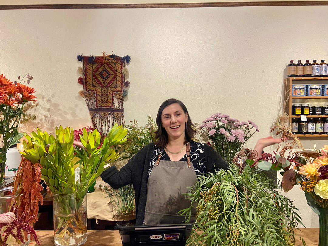 Shop Keeper, Christiana, at counter of Hawthorne shop, surrounded by flowers