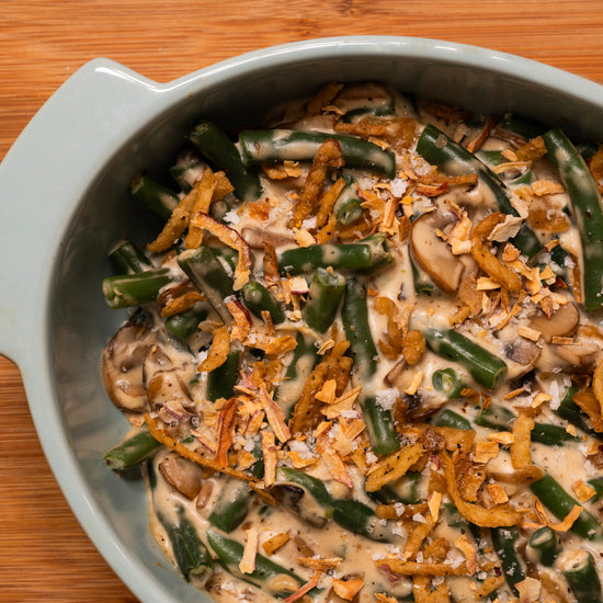 Green bean casserole with mushrooms and onions and crispy shallot salt in a gray dish on a wooden surface