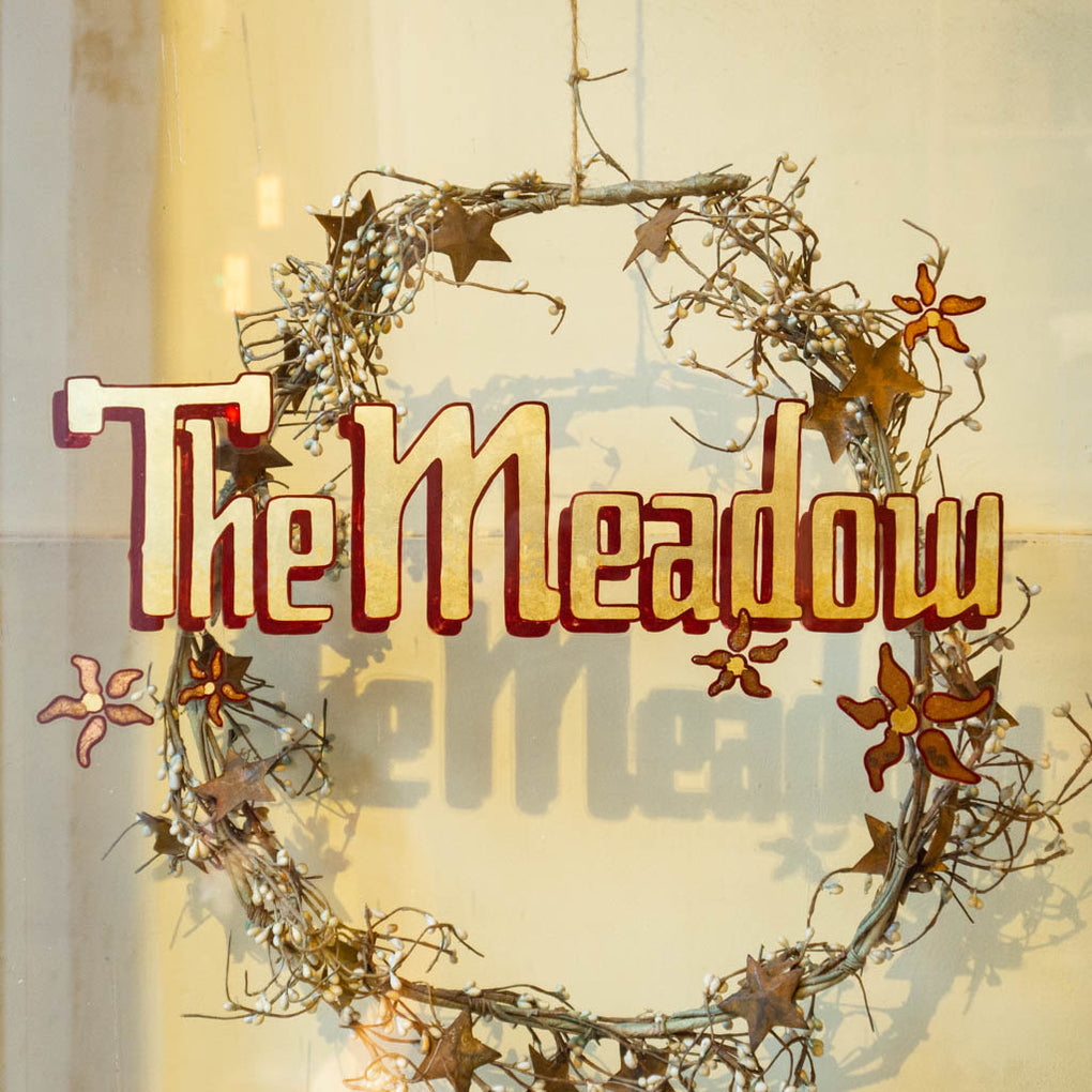 The Meadow Logo on a glass door at the shop, with a wreath in the background