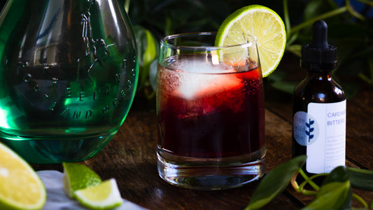 red cocktail with lime next to gin in green bottle