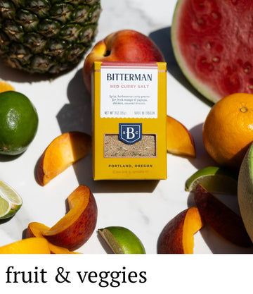 Bitterman's Red Curry Salt packaging surrounded by fruits and vegetables on a white background