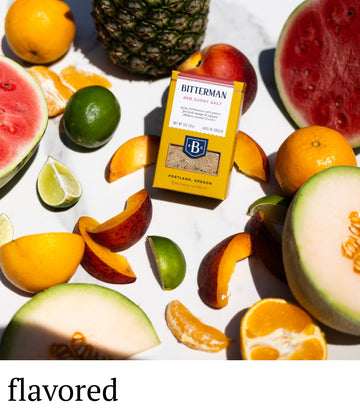 Bitterman's honey mustard packaging surrounded by assorted fruits on a white surface.