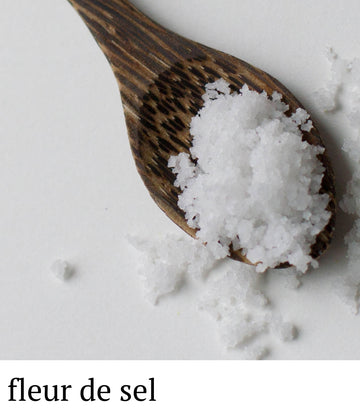 Wooden spoon filled with fleur de sel salt on a light background