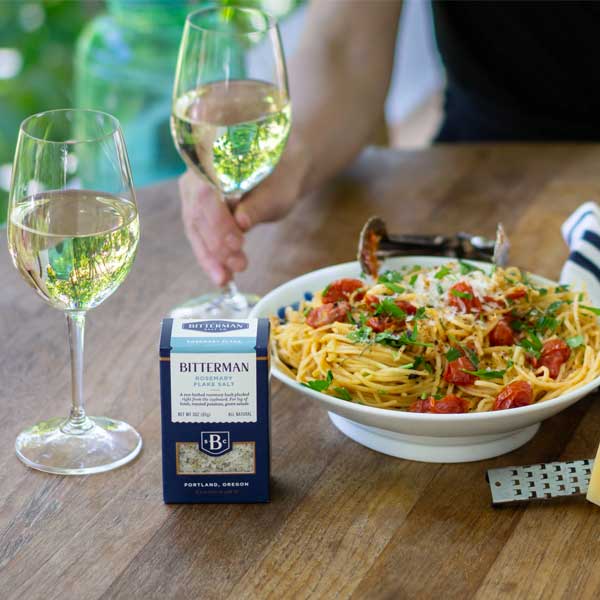 bowl of pasta and two glasses of white wine with rosemary flake salt