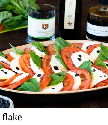Caprese salad with tomatoes, mozzarella, and basil in a bowl with wine bottles in the background.