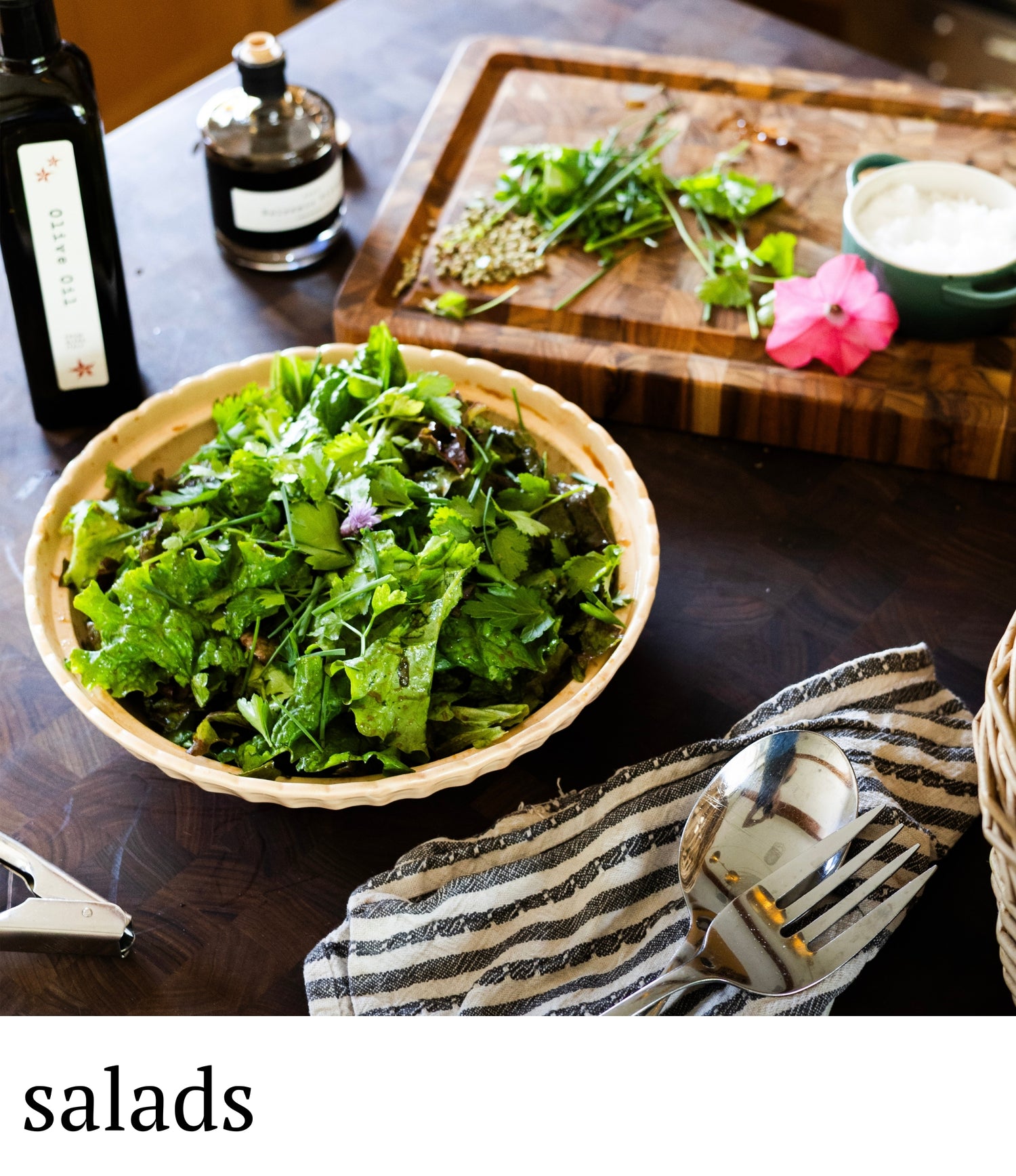 Bowl of salad on a wooden table with a cutting board and bottles in the background.