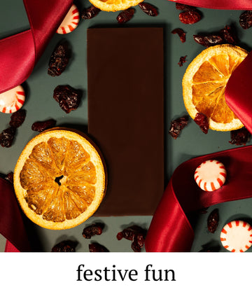 Dark chocolate bar surrounded by dried oranges, cranberries, and peppermint candies on a dark background with 'festive fun' text.