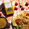 Bitterman's Yellow Curry Salt on colorful tablecloth next to noodle dish and cherry tomatoes