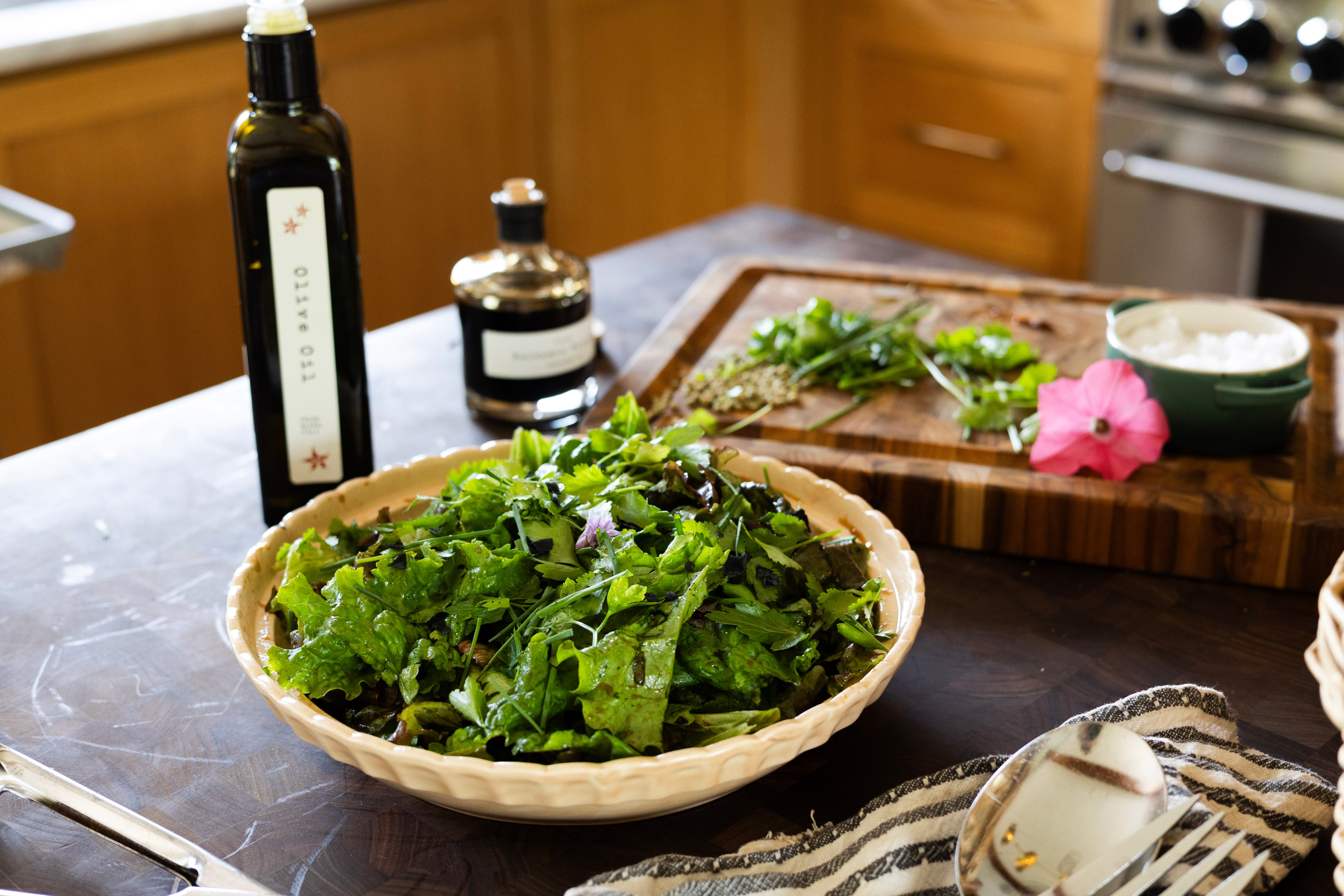lush green salad in bowl on a kitchen butcher block island next to olive oil and balsamic vinegar