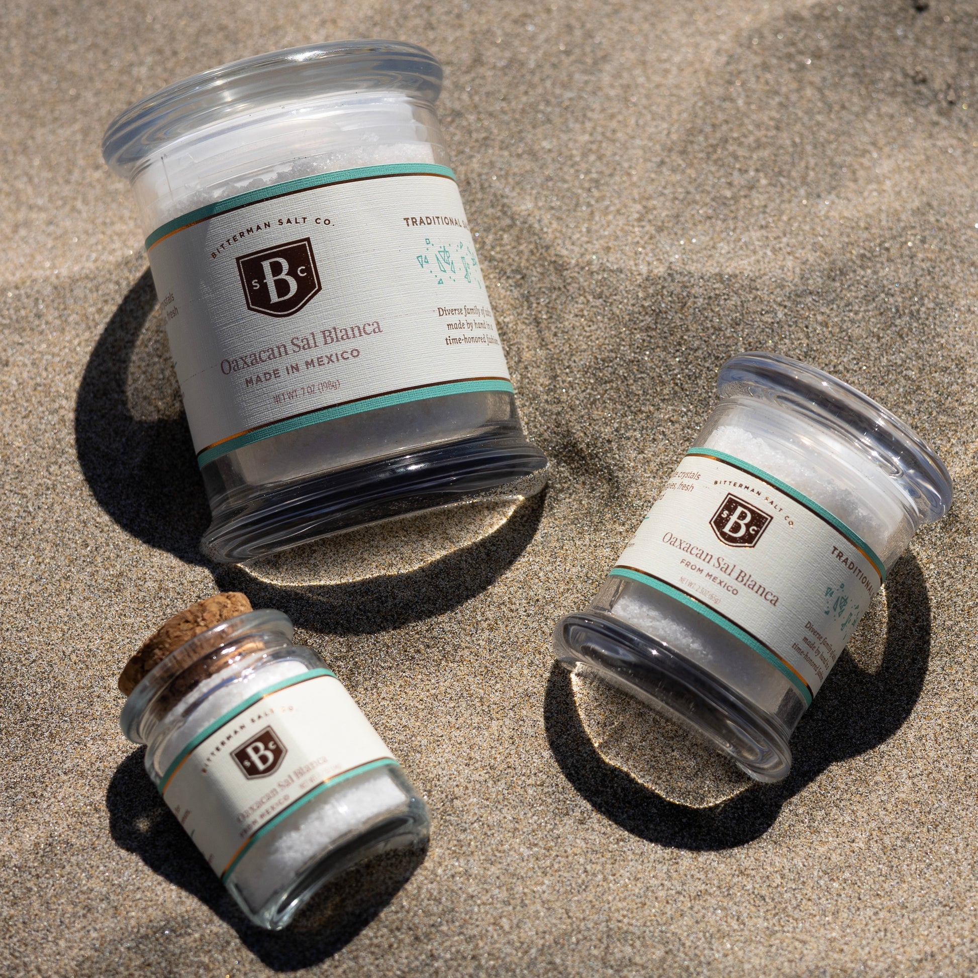 Three glass jars with labels on a sandy surface