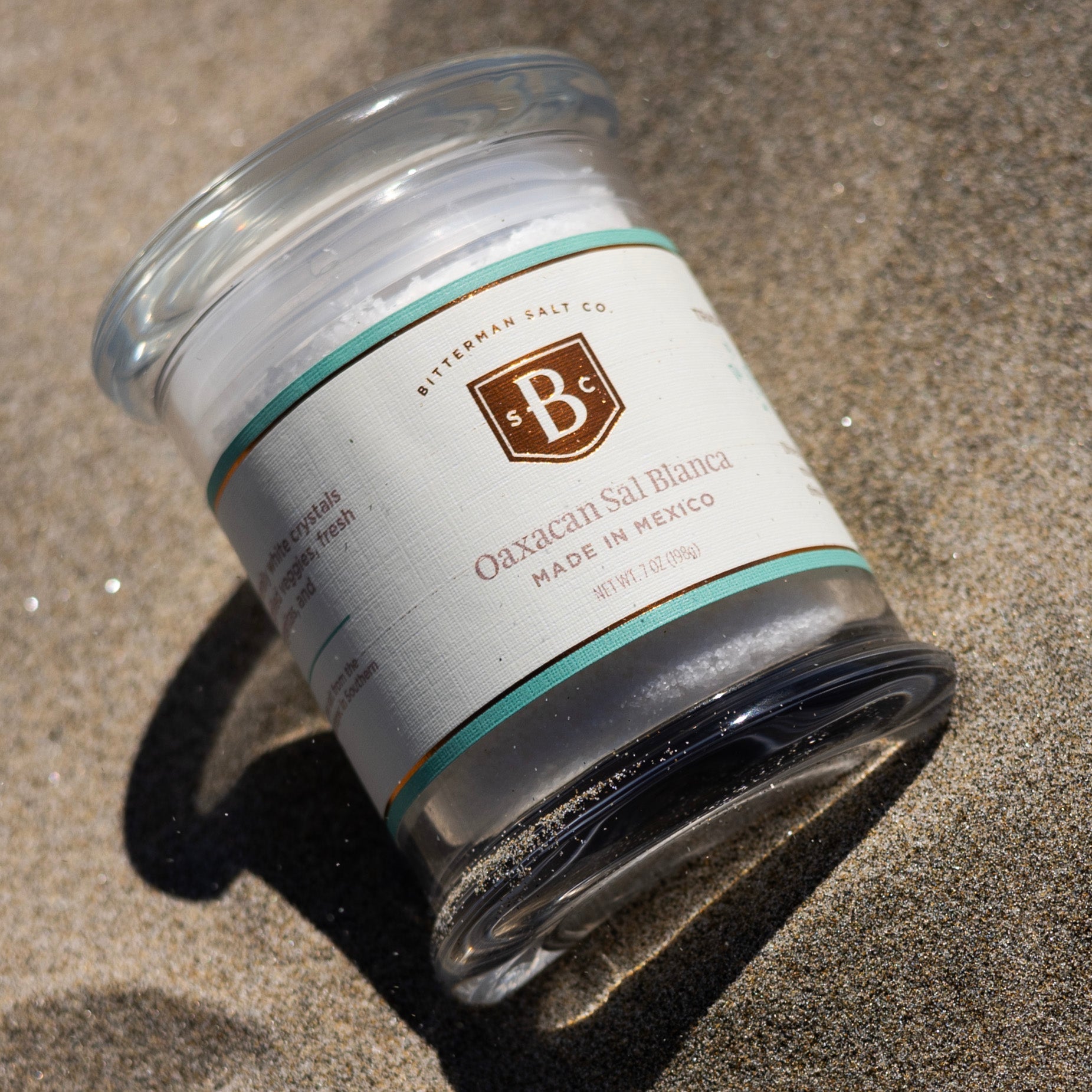 Jar of Gaxacan Sal Blanca salt with a visible brand label on a sandy surface