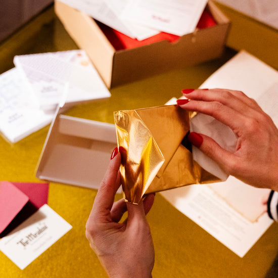 Person holding a gold foiled chocolate with additional chocolate club contents scattered on a yellow surface