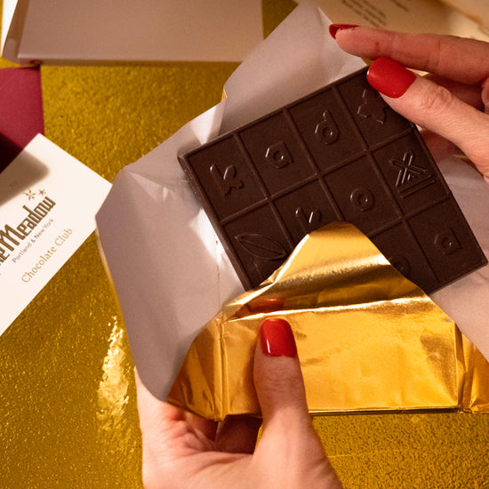 Chocolate bar with gold foil being held by a hand on a gold surface