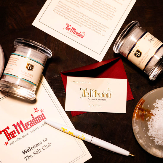 Salt club items with 'The Meadow' branding, including jars, a pen, and a card on a dark surface.