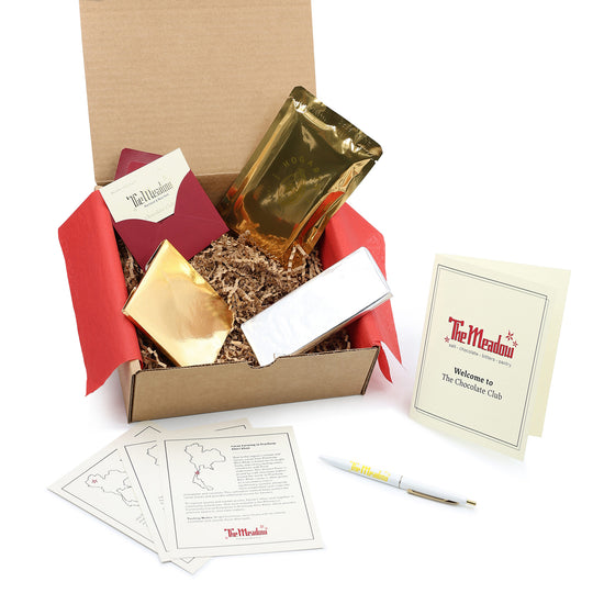 chocolate club box with membership card two gold and one silver foiled chocolate bars and informational materials and a pen