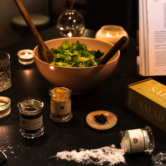 Table setting with a bowl of salad, small containers, and a book on a dark surface.