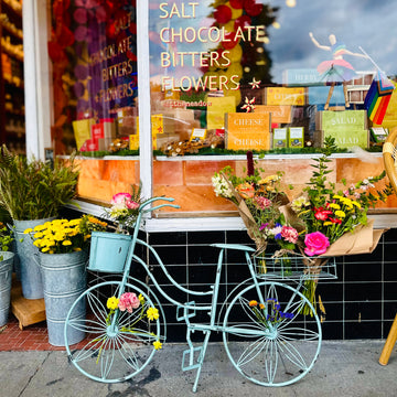 Decorative bicycle with flowers in front of a store window displaying products.