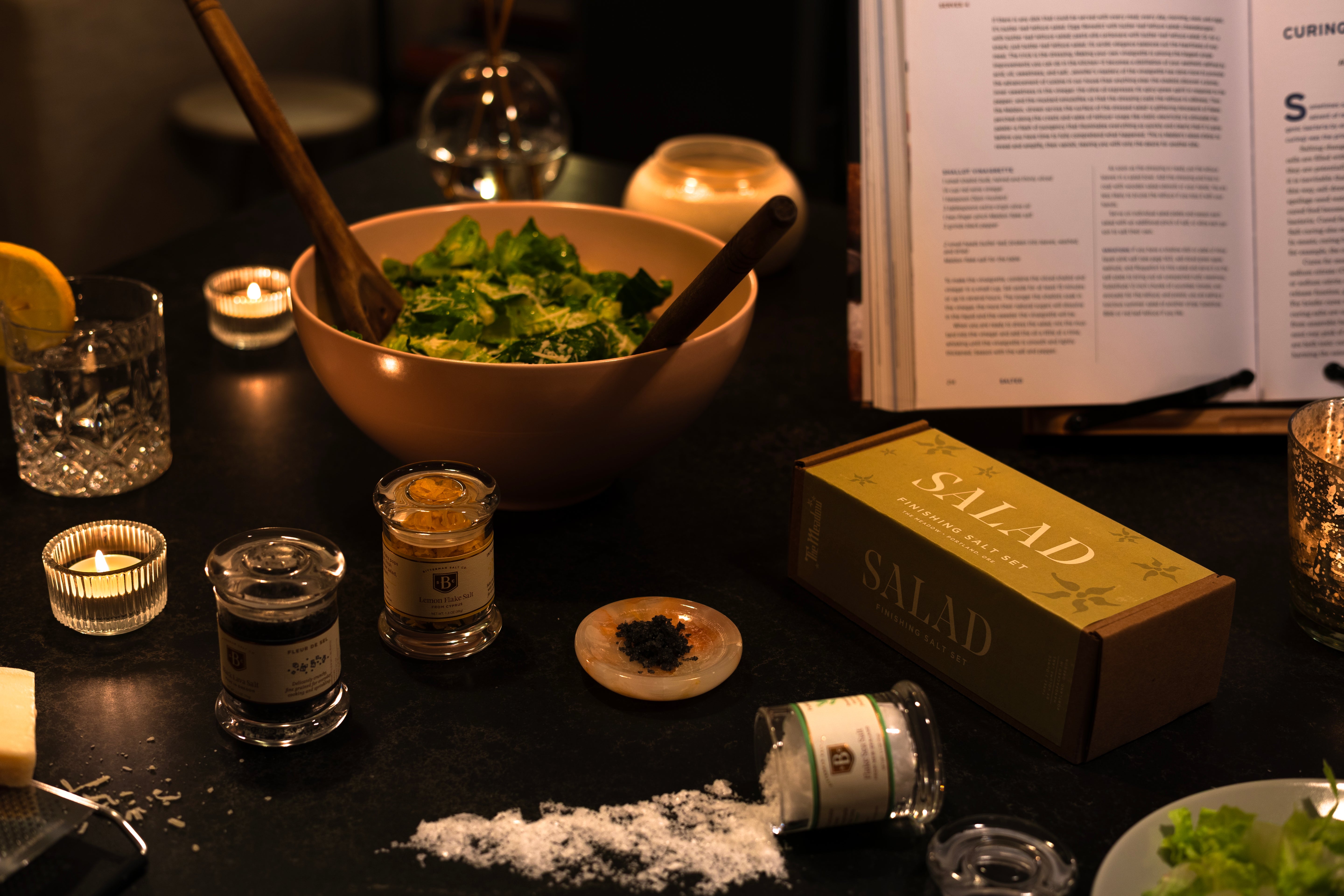 A salad in pink bowl on black table next to Meadow Salad salt set and Bitterman salts on table