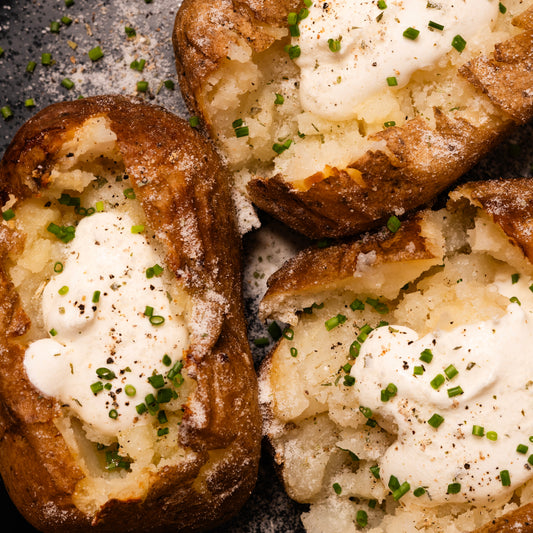 Baked potatos with sour cream and chives and sour cream and onion salt on a dark surface