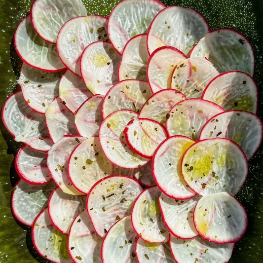 Sliced radishes arranged in a circular pile on a dark green platter, drizzled with olive oil and sprinkled with Bitterman x Barnacle Kelp Flake Salt