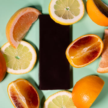 Dark chocolate bar surrounded by sliced citrus fruits on a light green background