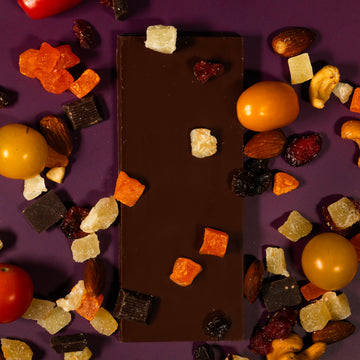 Chocolate bar surrounded by various dried fruits and nuts on a purple background