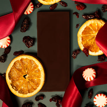 Dark chocolate bar with dried oranges, raisins, and peppermints on a dark surface.