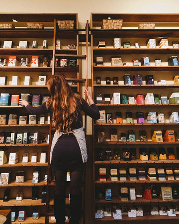 shop keeper rearranging merchandise on the wooden shelves of the chocolate wall on library ladder