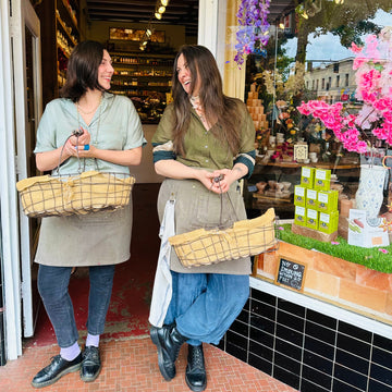 Two women standing outside a store with baskets, smiling.