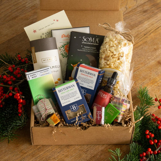 a gift box filled with misc treats on a wood floor with pine and berries