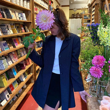 customer holding pink dahlia in front of their face; chocolate shelves in the background 